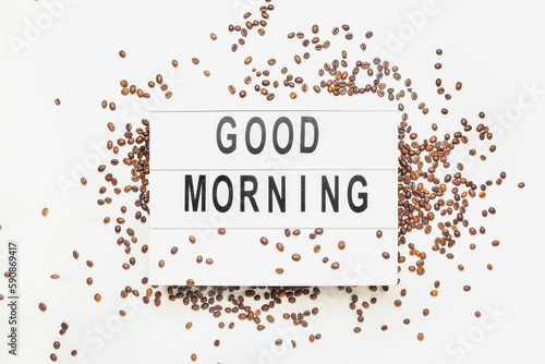 Board with text GOOD MORNING and coffee beans on light background