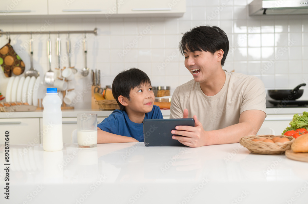 Young Asian father and his son using digital tablet enjoying together in kitchen at home