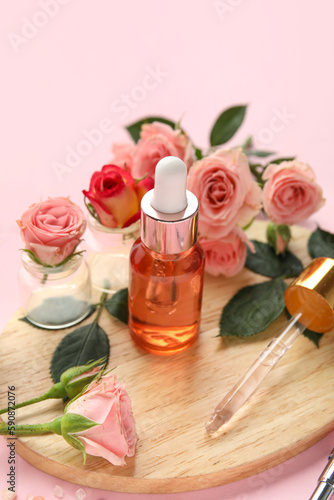 Wooden board with bottle of cuticle oil and beautiful rose flowers on pink background, closeup