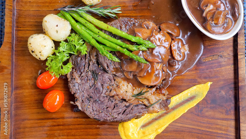 Top view of ribeye beef steak with grilled vegetables on a rustic wooden board. Angus ribeye beef steak cooked to perfection on the grill. Served with a side of grilled vegetables in restaurant.