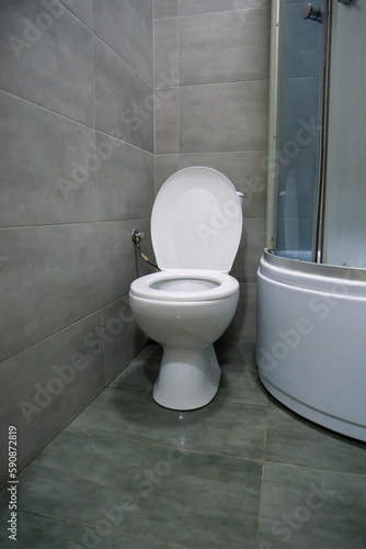 Toilet room interior with white toilet bowl, shower cabin, grey wall tiles