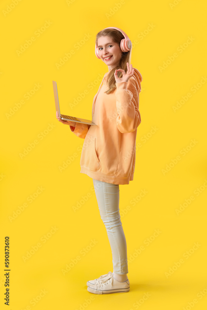 Fototapeta premium Female programmer in headphones with laptop showing OK on yellow background