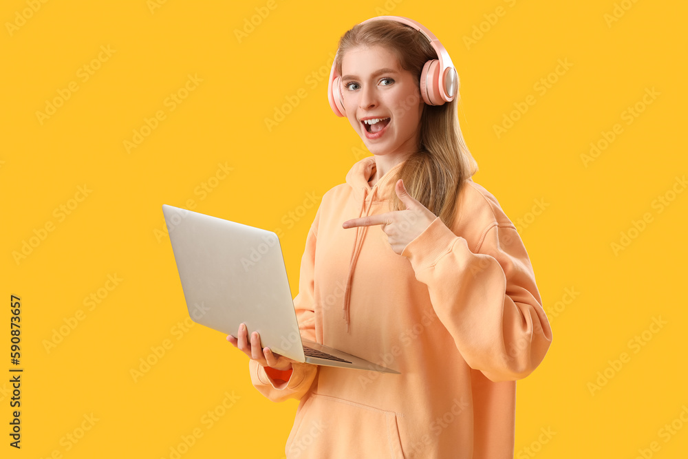 Female programmer in headphones pointing at laptop on yellow background Female programmer in headphones pointing at laptop on yellow background