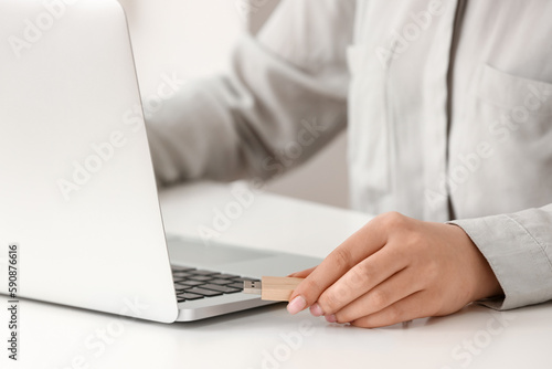 Woman using USB flash drive with modern laptop at light table  closeup