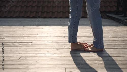Legs barefoot of woman in jeans on toes playfully approach legs of man and gently step on each other and dance their fingers. Wooden floor, illuminated by sunlight and shadows from couple in love. photo