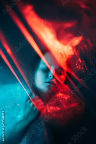 Plastic pollution. Global warming. Ecology problem. Red blue color light defocused exhausted woman suffocating suffering from shortness of breath wrapped in polyethylene film.
