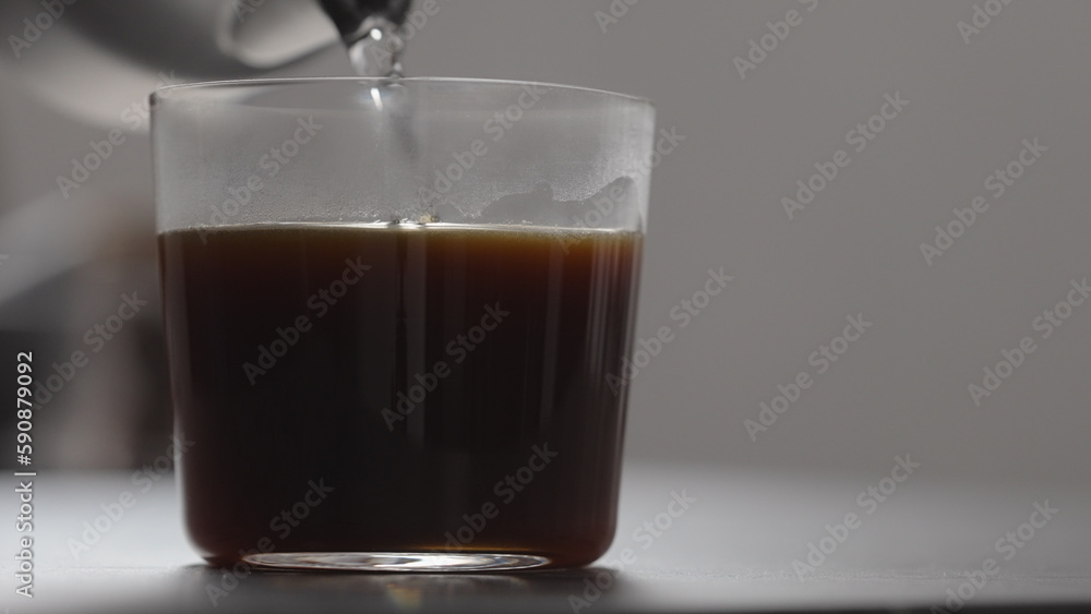 pour water in coffee in tumbler glass on concrete countertop with copy space