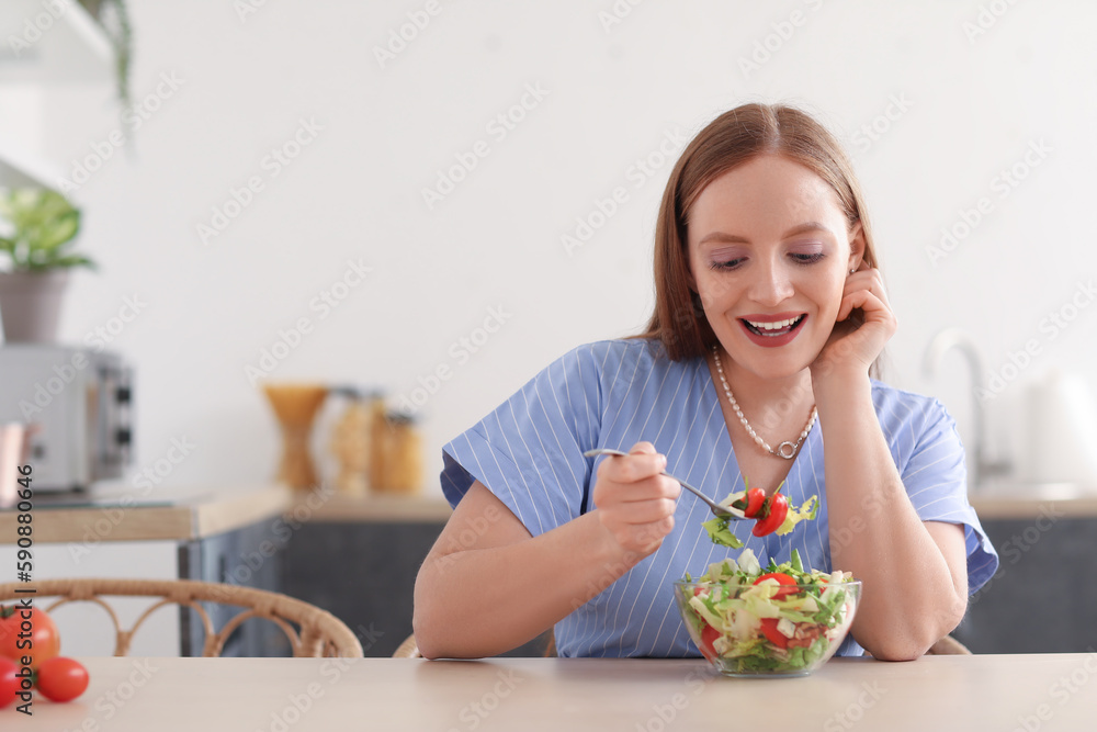 Young woman eating vegetable salad at table in kitchen Young woman eating vegetable salad at table in kitchen