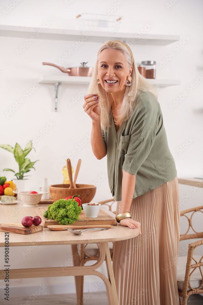 Mature woman making vegetable salad at table in kitchen
