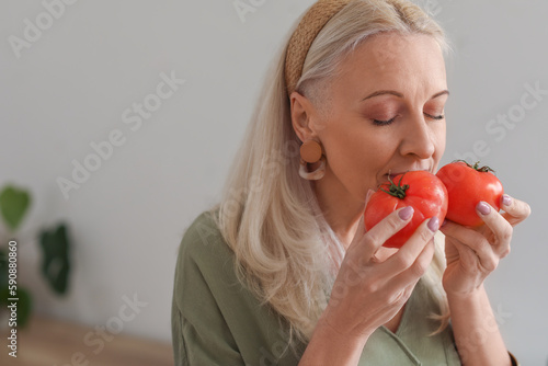 Mature woman with fresh tomatoes in kitchen, closeup