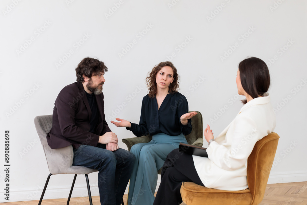 Fototapeta premium Concept of marital therapy. A female psychologist sits with her back to the camera and listens to the family couple during therapy session