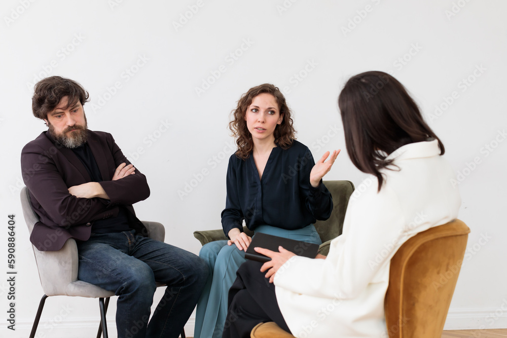 Obraz premium Concept of marital therapy. A married couple quarrels during therapy in front of a psychologist sitting with her back to the camera