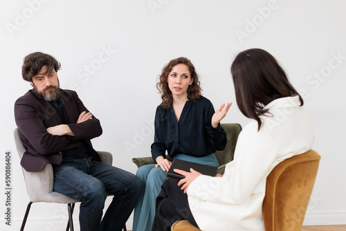 Concept of marital therapy. A married couple quarrels during therapy in front of a psychologist sitting with her back to the camera