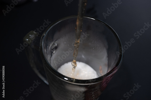 A stream of beer pours into a glass. Dark background.