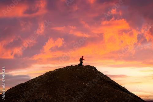 Hiker standing on top of volcanic mountain with colorful sky in the sunset among Icelandic Highlands in summer