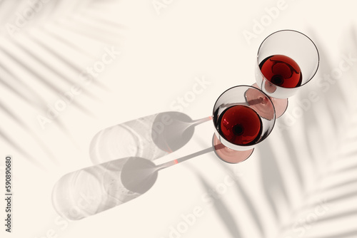 Minimal summer flat lay with glasses of red wine, sunlight shadow, palm leaf shade on beige background, Two wine glasses, alcohol drinks photo Holidays, parties, events, relaxation concept photo