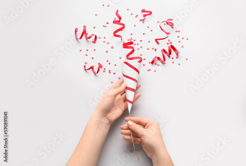 Fotografija Female hands with party popper and confetti on light background