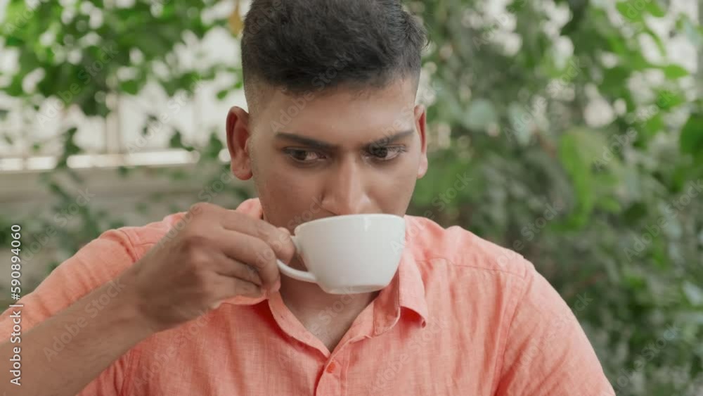 Tilt up shot of young Indian man drinking cappuccino and having discussion with friend while eating out in cafe Tilt up shot of young Indian man drinking cappuccino and having discussion with friend while eating out in cafe