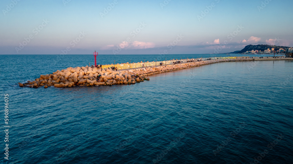 aerial view from the drone of the port of Pesaro with the rocks and people watching the sunset