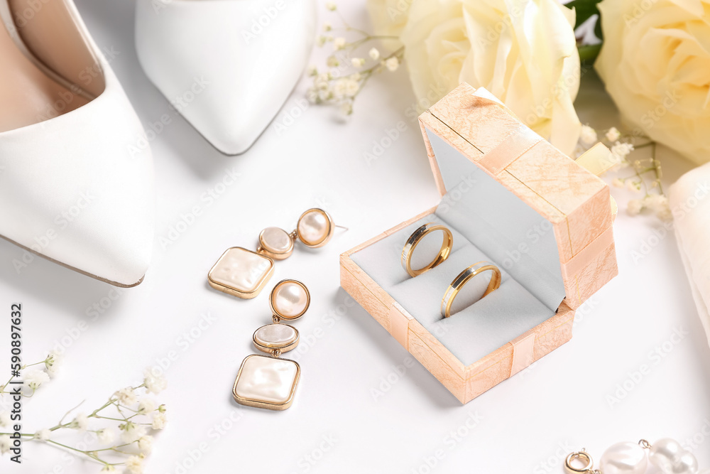 Box with wedding rings, earrings, heels and flowers on white background, closeup