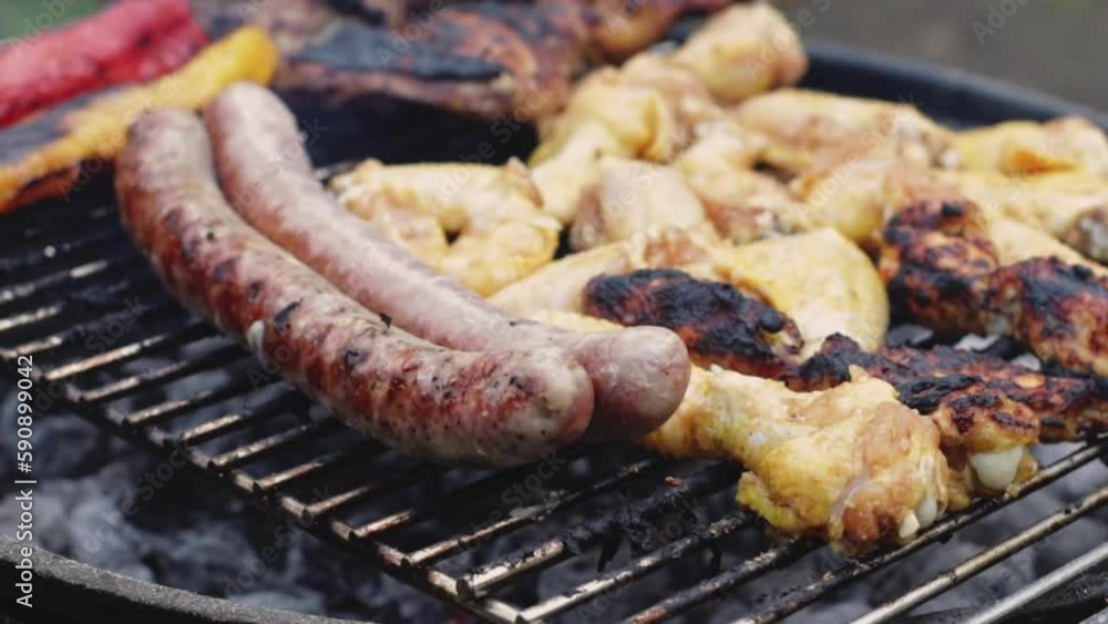 Delicious and appetizing grilled sausages with chicken wings on a grill in the backyard of the house, close-up side view in slow motion with zoom out. Delicious and appetizing grilled sausages with chicken wings on a grill in the backyard of the house, close-up side view in slow motion with zoom out.