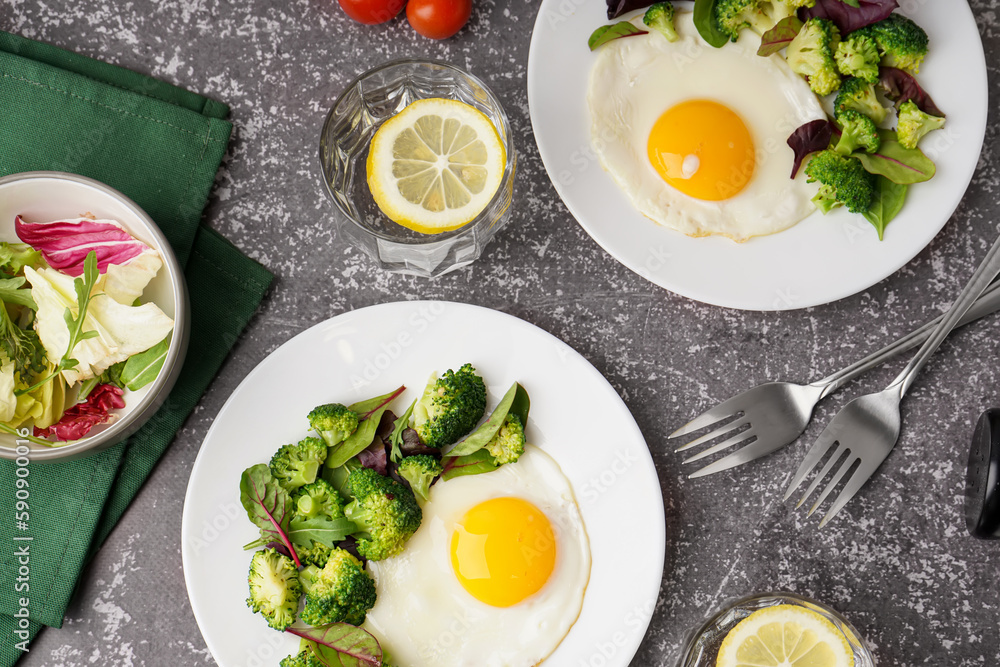Plates with tasty fried eggs, broccoli and spinach on grey grunge background Plates with tasty fried eggs, broccoli and spinach on grey grunge background