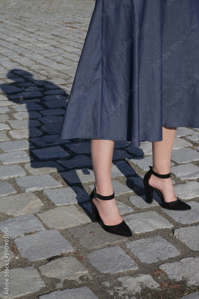 Woman in midi blue dress and pointed toe pumps with block high heels and ankle strap on the cobblestone street Woman in midi blue dress and pointed toe pumps with block high heels and ankle strap on the cobblestone street