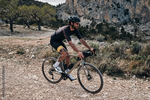 Man riding gravel bike on gravel road in mountains with scenic view.Professional cyclist practicing on gravel road.Male cyclist wearing black cycling kit and helmet.Cycle camp in Calpe, Alicante,Spain