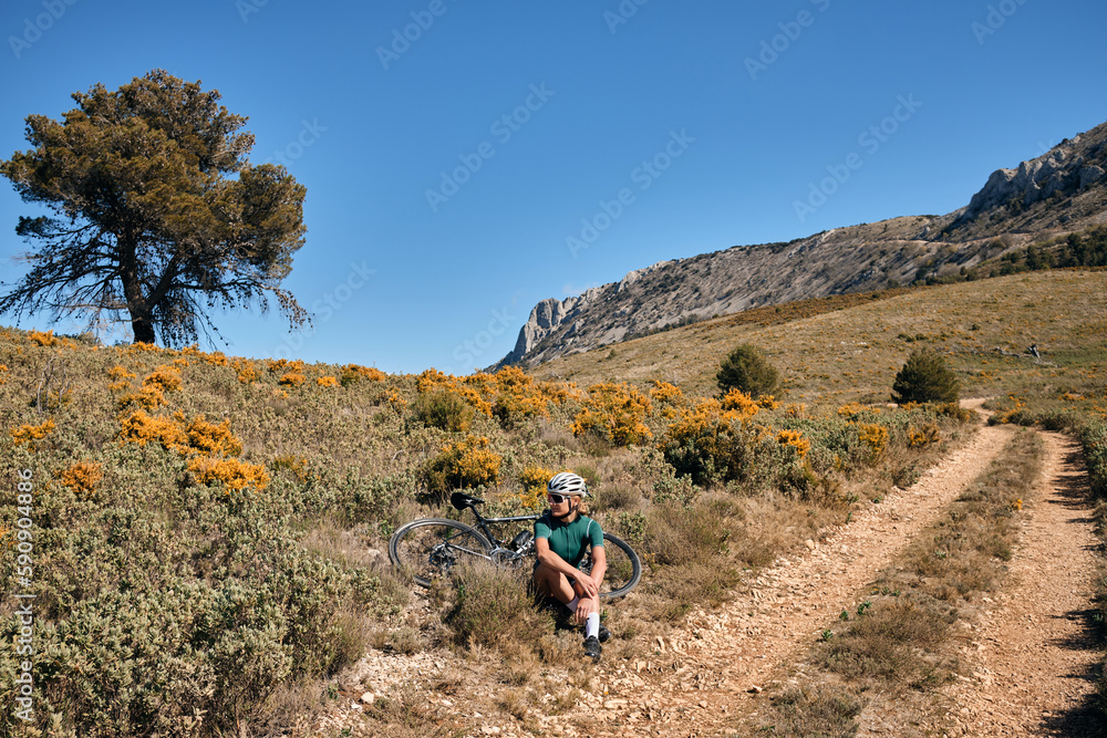 Woman cyclist wearing cycling green jersey, black shorts and helmet resting during training on the bicycle in the mountains.Spanish mountain landscapes.