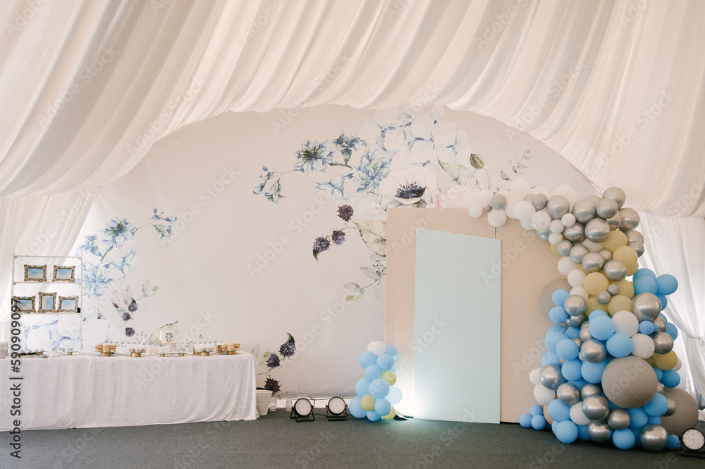 A large photo zone with blue and white balloons and a candy bar in a white tent