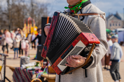 Gentleman musician plays a red accordion at a traditional Baltic cultural event wearing traditional wool outfit un grey color