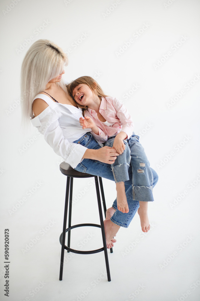 Laughing baby girl 4-5 year old on mother hands sitting on wooden chair over white background. Motherhood.