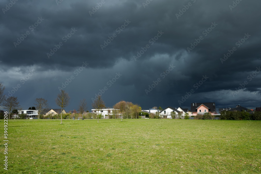 Obraz premium scary natural dark storm clouds in the sky with a housing estate at the straight horizon