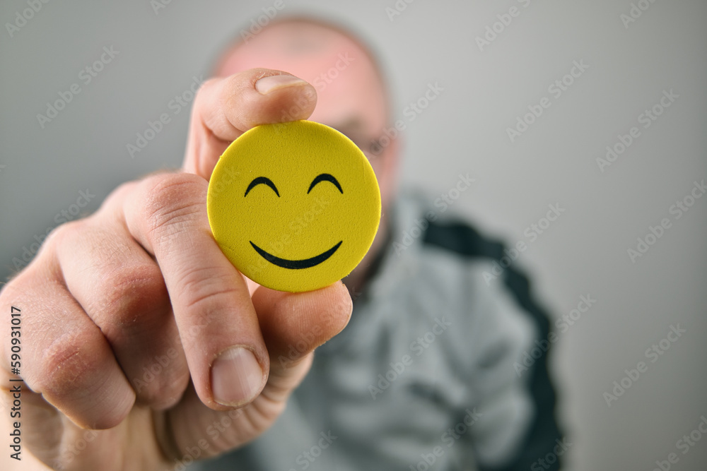 Person holding yellow smiley face emoji in front of his face