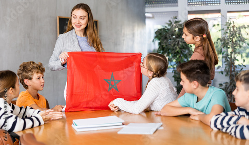 Group of preteen schoolchildren attentively watching teacher describing Morocco flag in schoolroom