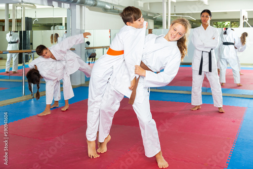 Teenager boy and girl, working in pair, mastering new karate moves in class with trainer