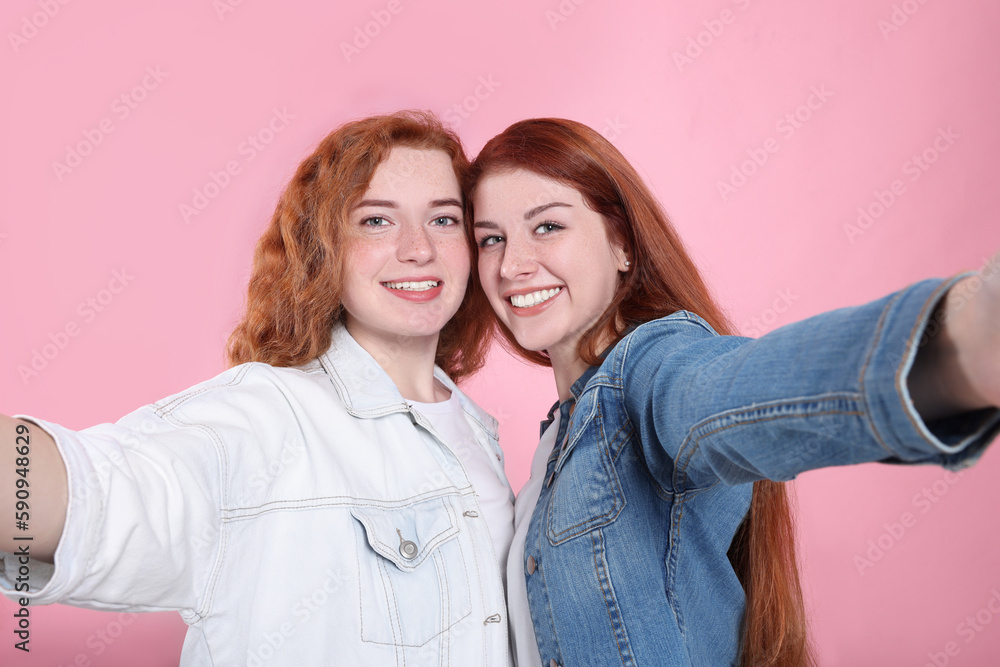 Beautiful young redhead sisters taking selfie on pink background Beautiful young redhead sisters taking selfie on pink background