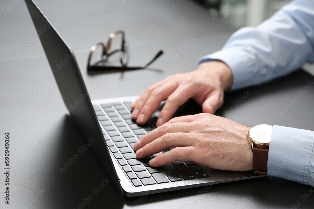 Man working on laptop at black desk in office, closeup Man working on laptop at black desk in office, closeup