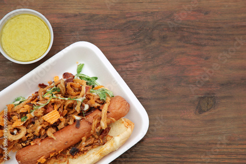 Fresh delicious hot dog with sauce on wooden table, flat lay. Space for text