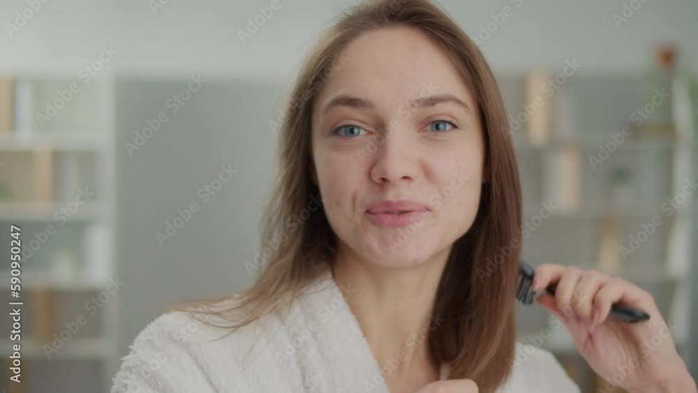 Portrait of a Smiling Young Woman Combing Her Hair at Home. Happy Woman, Wearing a Bathrobe, Brushing Her Hair in the Morning Getting Ready for Her Everyday Routine. Healthy Hair Concept. Portrait of a Smiling Young Woman Combing Her Hair at Home. Happy Woman, Wearing a Bathrobe, Brushing Her Hair in the Morning Getting Ready for Her Everyday Routine. Healthy Hair Concept.