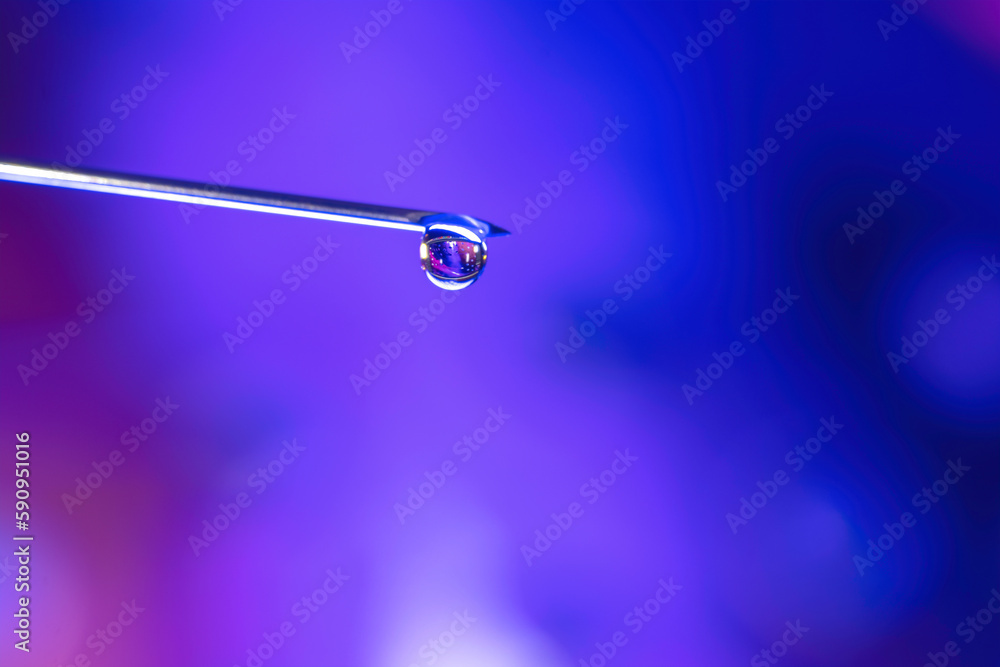Macro of a liquid drop at the end of a syringe needle, blue background, nobody Macro of a liquid drop at the end of a syringe needle, blue background, nobody