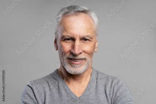 Closeup portrait of smiling senior man with beard and gray hair looking at camera isolated on gray background. Health care, dental concept 