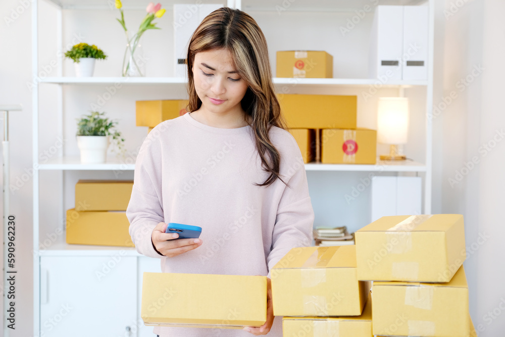 Young asian woman ,small business owner scaning product stock by mobile phone at home office Young asian woman ,small business owner scaning product stock by mobile phone at home office