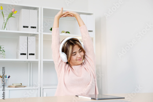 Young asian woman with headphones stretching for relax after working