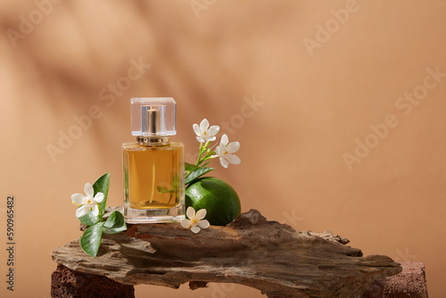 Close up view of a tree branch with Lime, several white flowers and a perfume glass bottle containing yellow liquid of Lime (Citrus aurantiifolia) extract. Empty label for branding mockup photo