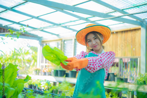 Beautiful asian farmer wearing apron and straw hat standing holding organic vegetables and lodge to the left with smile on her face, Smart farm.