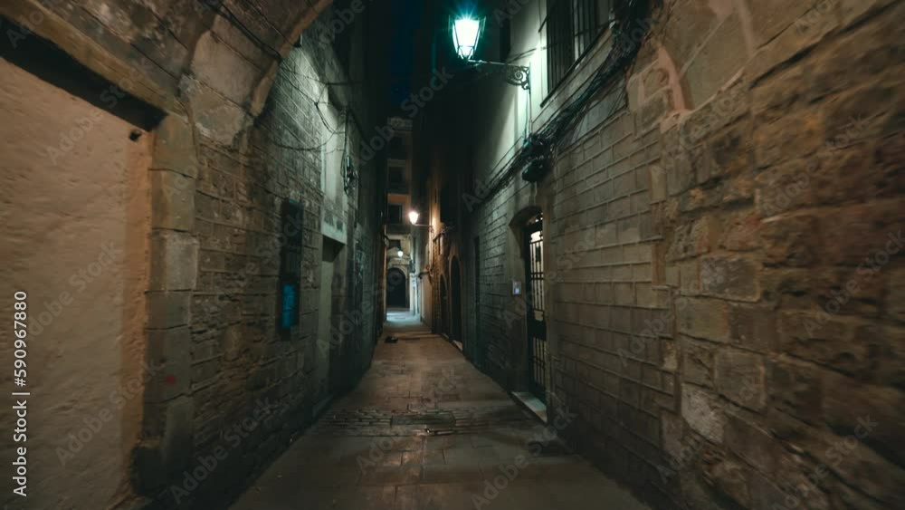 Urban dark empty street with graffiti; glowing white street lights; city of Barcelona, El Born, Gothic quarter, Catalonia, Spain; distant people walking by slowly; evening time in Spanish city centre Urban dark empty street with graffiti; glowing white street lights; city of Barcelona, El Born, Gothic quarter, Catalonia, Spain; distant people walking by slowly; evening time in Spanish city centre