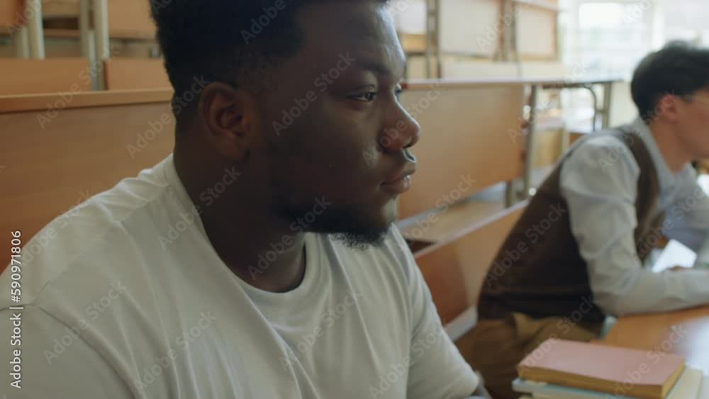Selective focus shot of young Black male student making notes during lecture in university Selective focus shot of young Black male student making notes during lecture in university