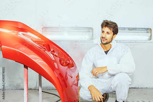 Fényképezés Portrait handsome skilled painter technician professional white uniform sitting and admiring the masterpiece job painted red fiberglass car front bumper successfully repaired in the paint room