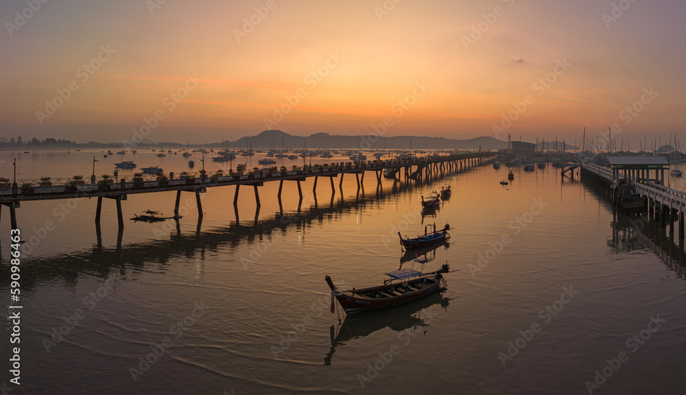 aerial view fishing boats on the beach at Chalong pier in sunrise..Sunrise with sweet yellow color light rays and other atmospheric effects..colorful reflection of sunrise in the sea background..d.